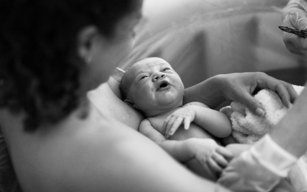 A mother looks at her newborn baby as he looks up at her.