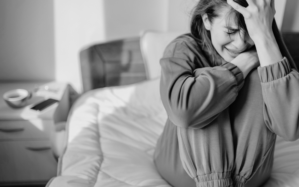 A crying woman sitting on her bed, coping with the emotional pain of IUFD loss.