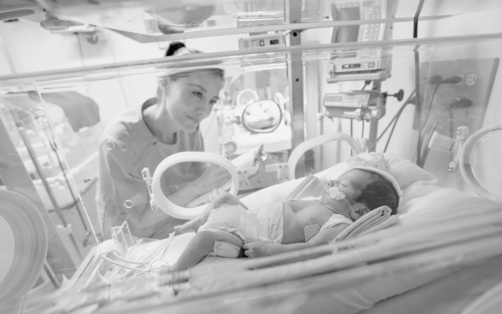 Mother looking at her baby in the NICU, connected to oxygen support.