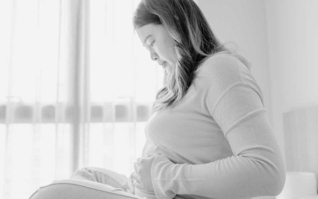 Pregnant woman holding her belly, looking concerned.